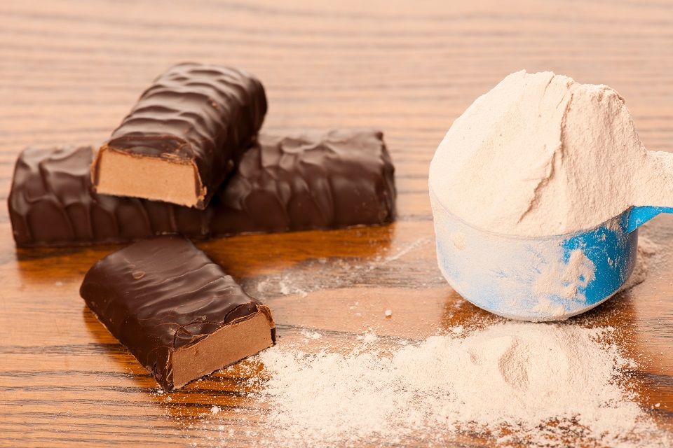 Whey protein powder in measuring scoop and chocolate protein bar