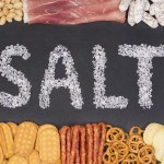 Word salt written with sea salt crystals surrounded by food containing a lot of salt