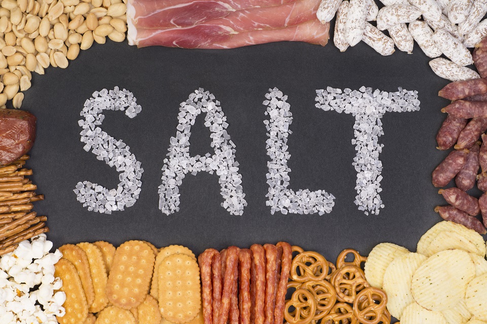 Word salt written with sea salt crystals surrounded by food containing a lot of salt