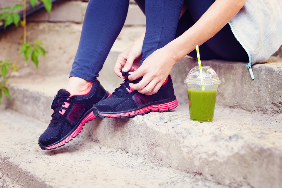 Green detox smoothie cup and woman lacing running shoes