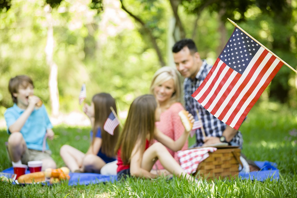 Family enjoys July 4th picnic in summer season. American flag.