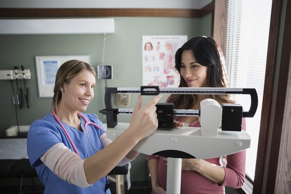 Nurse checking weight of pregnant woman