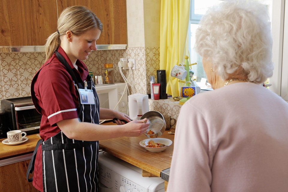 young Nurse cooking for senior woman in her kitchen