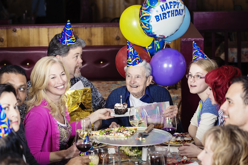 A group o people celebrating a birthday with pizza and cake
