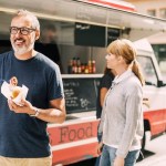 Mature man eating food while standing against truck at street