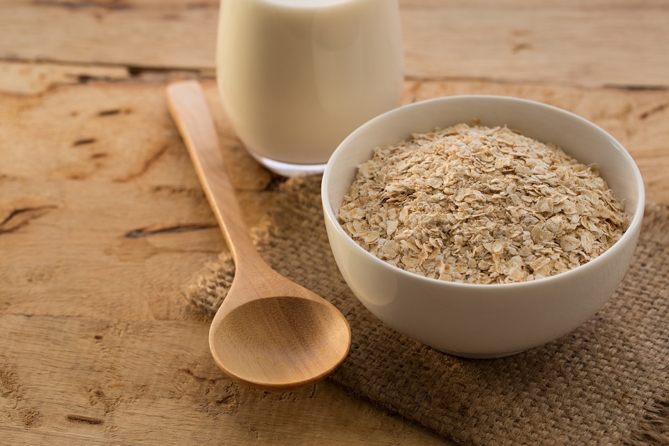 Close-Up Of Oats In Bowl By Wooden Spoon And Milk Glass On Table