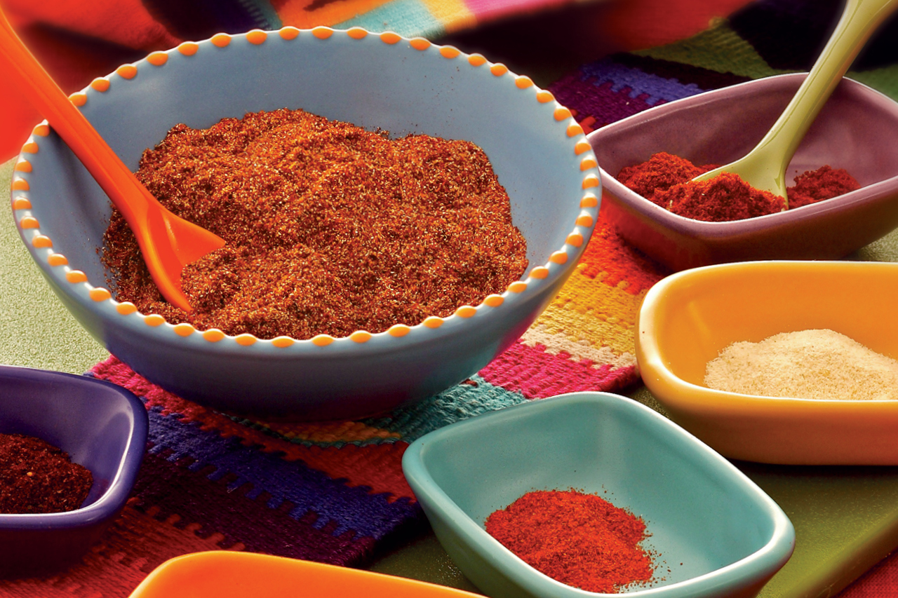 Various spices in colorful bowls with spoons.
