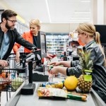 Mature Couple Putting Groceries On Conveyor At Checkout