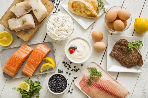 Chicken meat, fish, cottage cheese, yogurt and eggs on white table