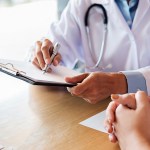 Midsection Of Doctor With Clipboard Discussing With Patient On Table