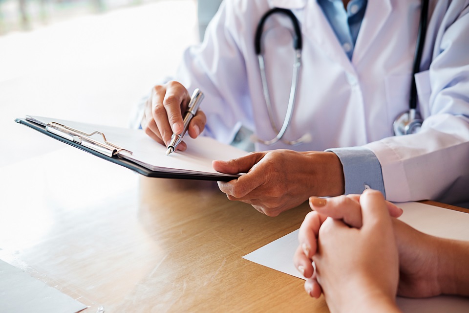 Midsection Of Doctor With Clipboard Discussing With Patient On Table