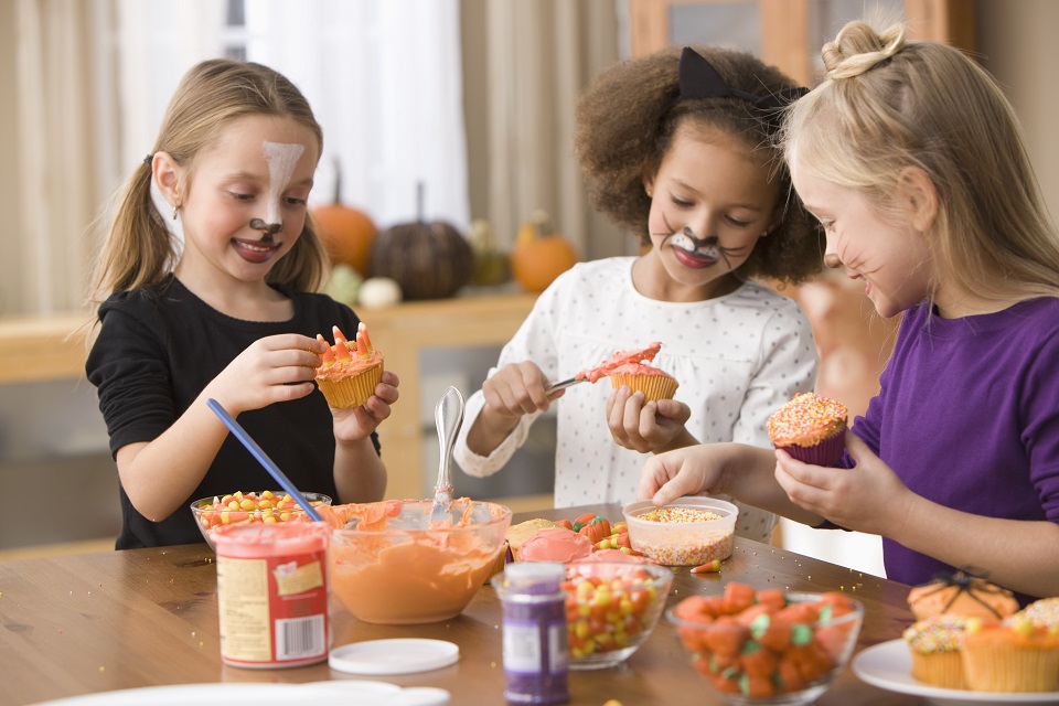 Girls in Halloween costumes decorating cupcakes