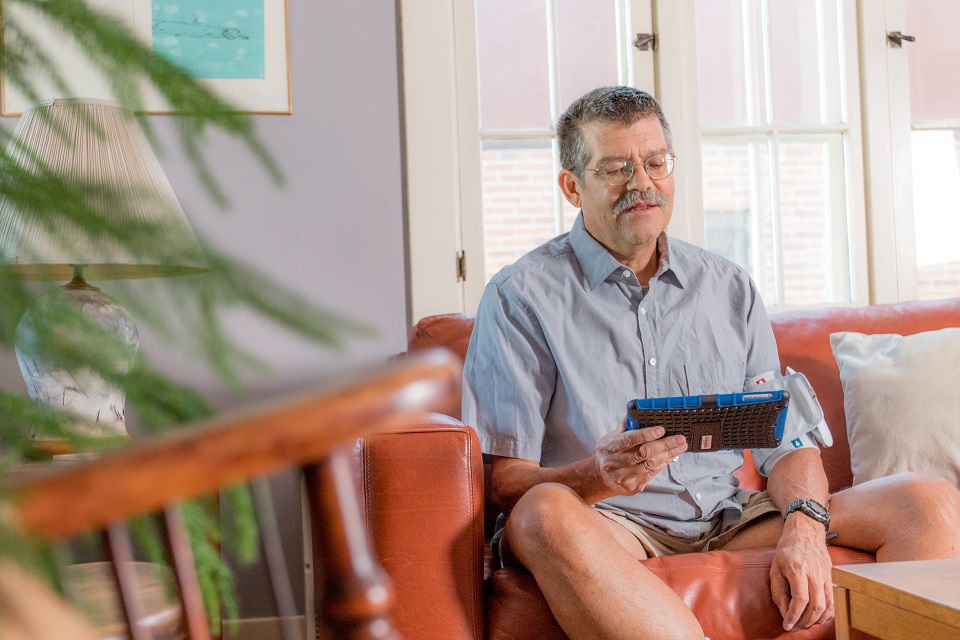 Home dialysis patient setting on a couch while using monitoring device.