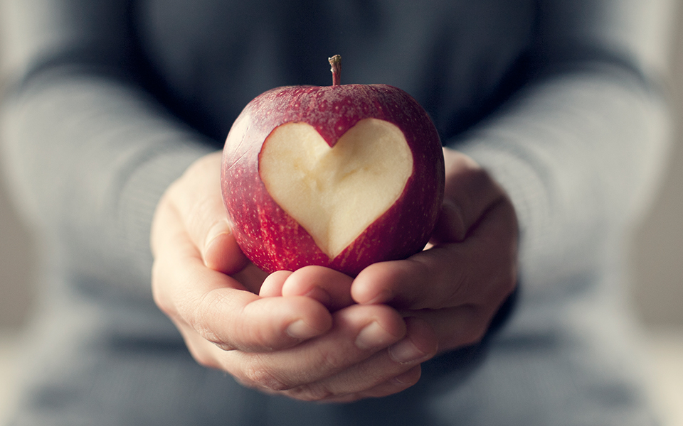 Hands holding an apple with heart shape carved into it.