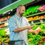 Man uses phone at grocery store to get more information about his purchases.