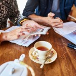 Midsection of couple calculating home finances. Young male and female partners doing paperwork. They are sitting at wooden table.