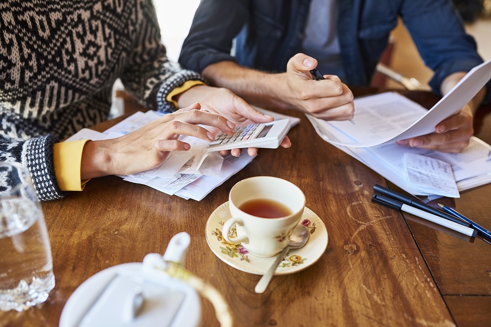 Midsection of couple calculating home finances. Young male and female partners doing paperwork. They are sitting at wooden table.