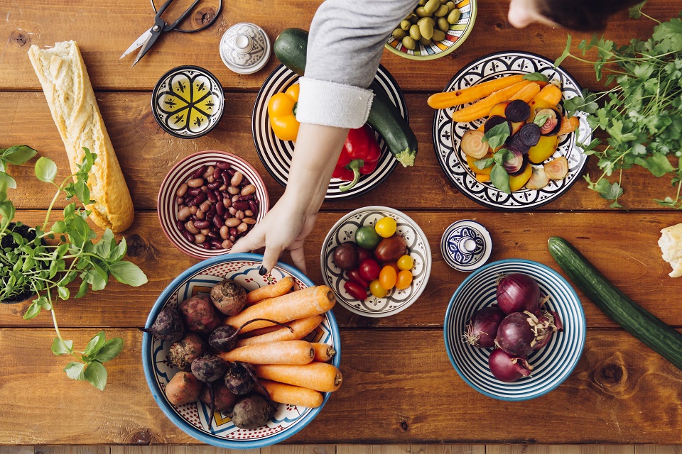 Cropped image of woman picking up vegetables at wooden table