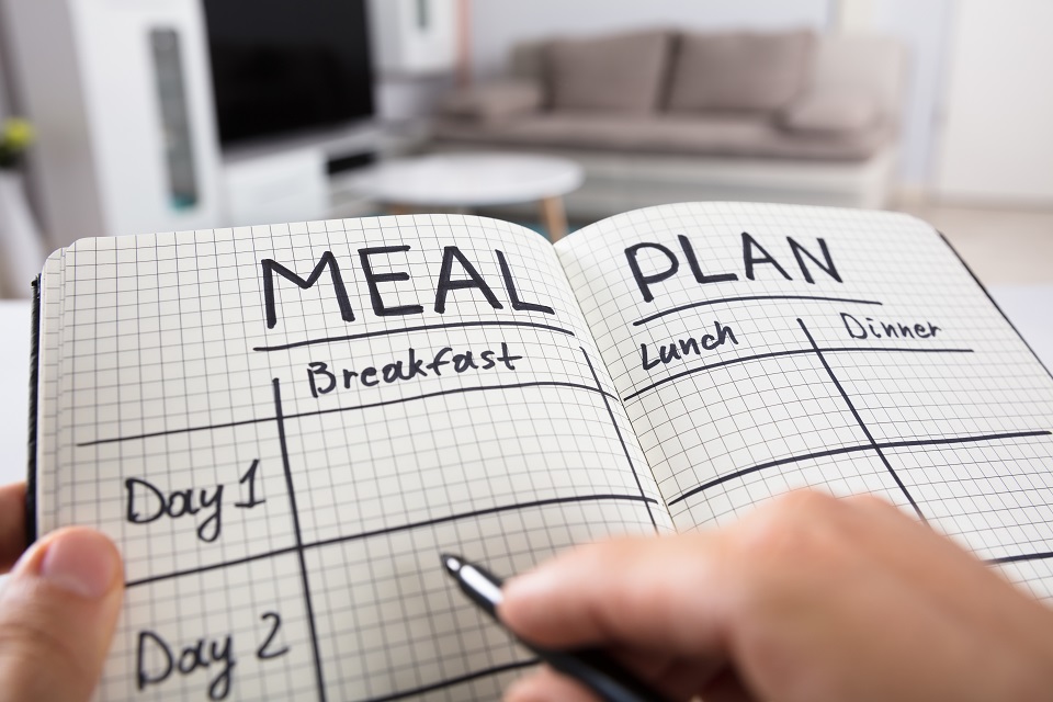 hand holding pen filling out meal plan in a notebook