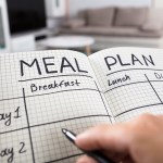 hand holding pen filling out meal plan in a notebook