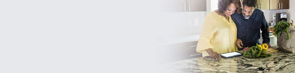 A man and woman looking at a recipe with vegetables in a bag on the table