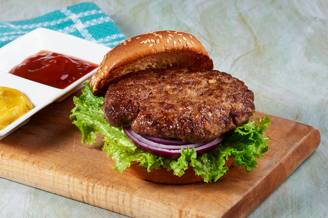 A burger on a cutting board with ketchup and mustard next to it in a bowl