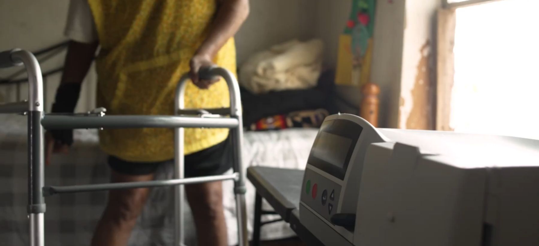 Woman wearing a yellow shirt standing by a dialysis machine with a walker