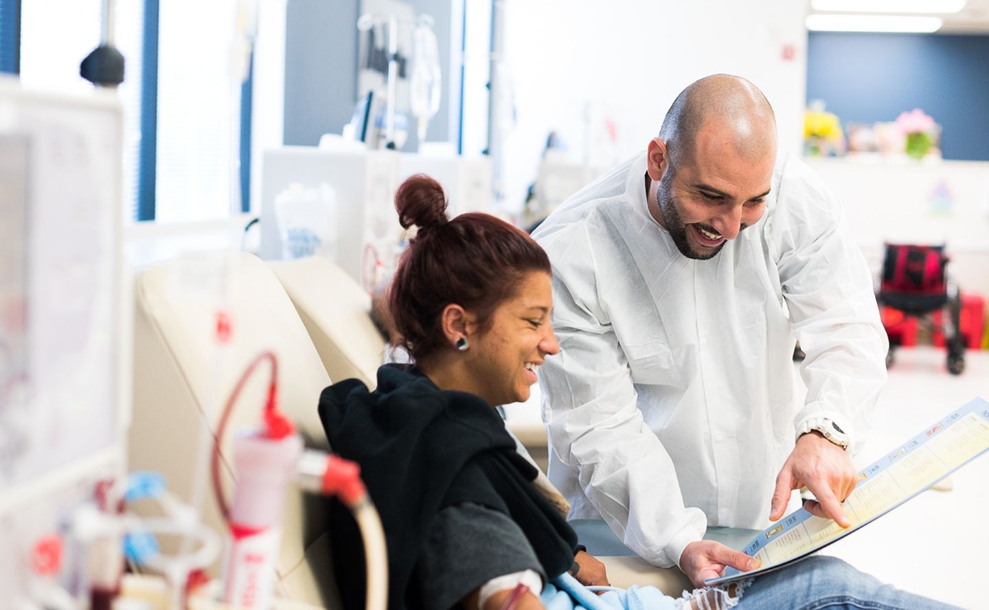 A DaVita care teammate reviewing a plan with a seated patient beside dialysis equipment